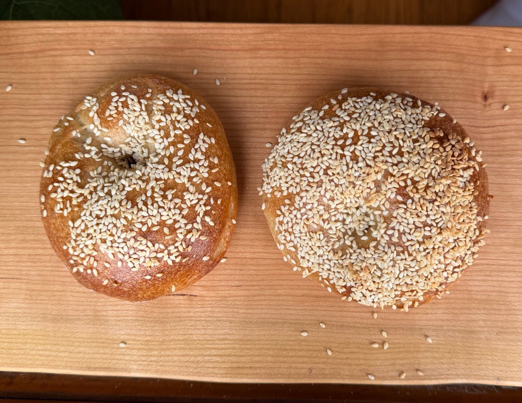 Two finished sesame bagels on a wooden board