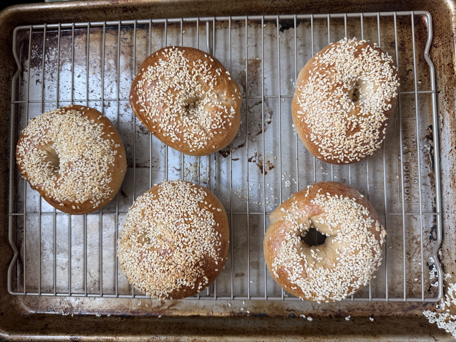 Golden, evenly baked sesame bagels cooling on a rack