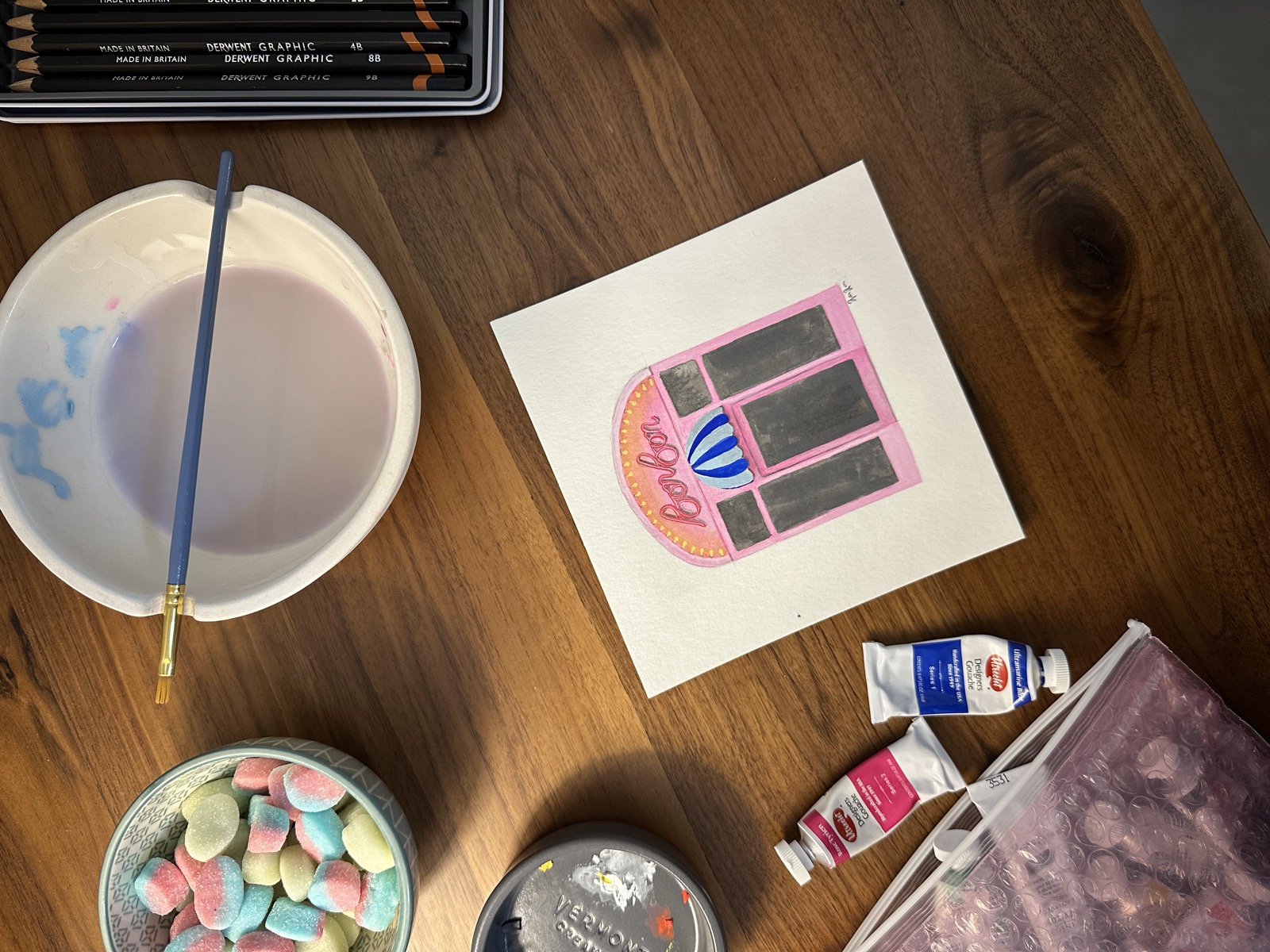 Gouache painting of the Bon Bon storefront, at the painter's workstation